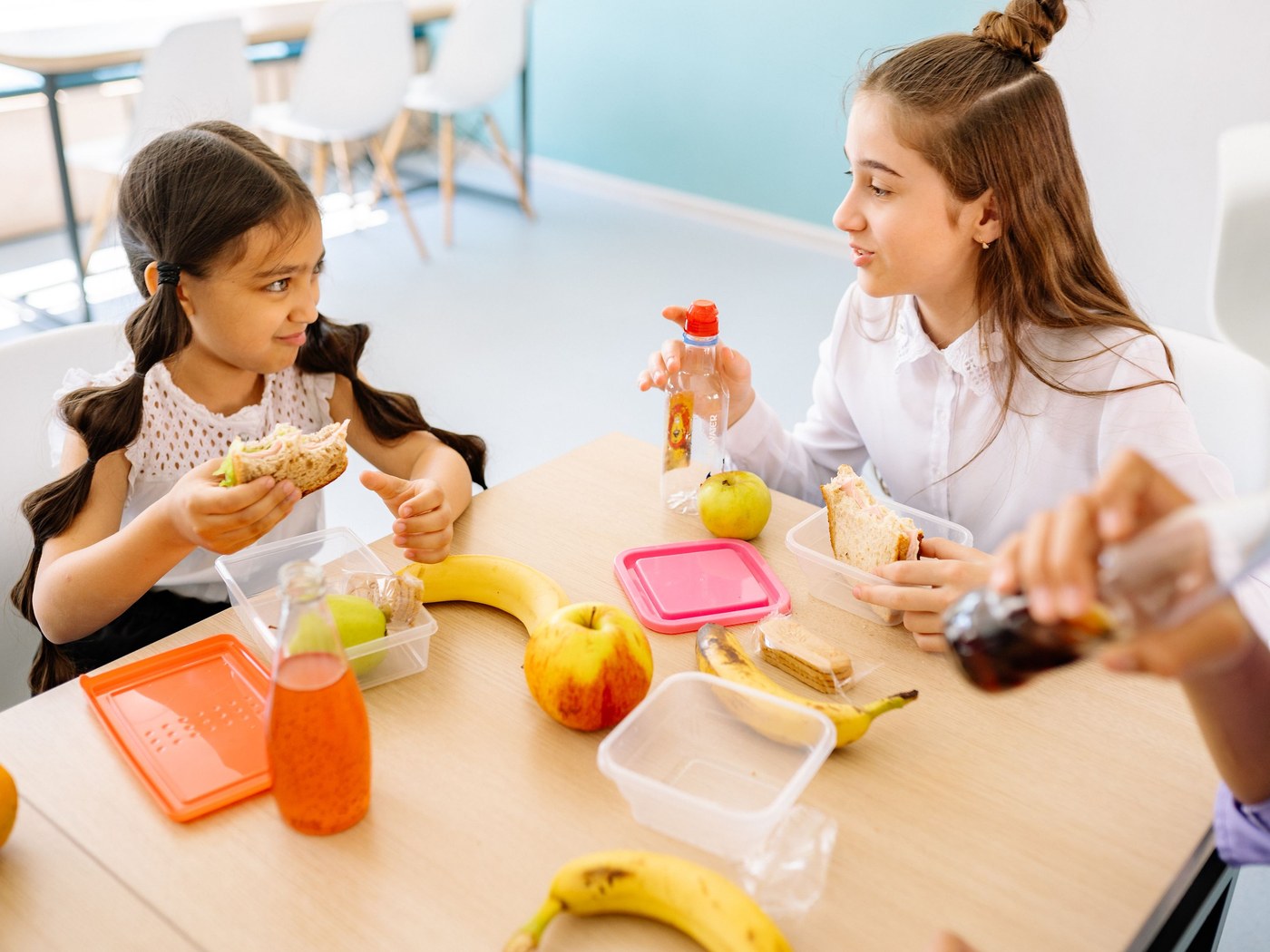 What a Great Neck social skills class looks like. Children at a table with lunch boxes and fruit, two of them turned toward each other talking while they eat.